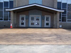 Brick building entrance with three white doors, a covered porch, and an orange traffic cone on the left.