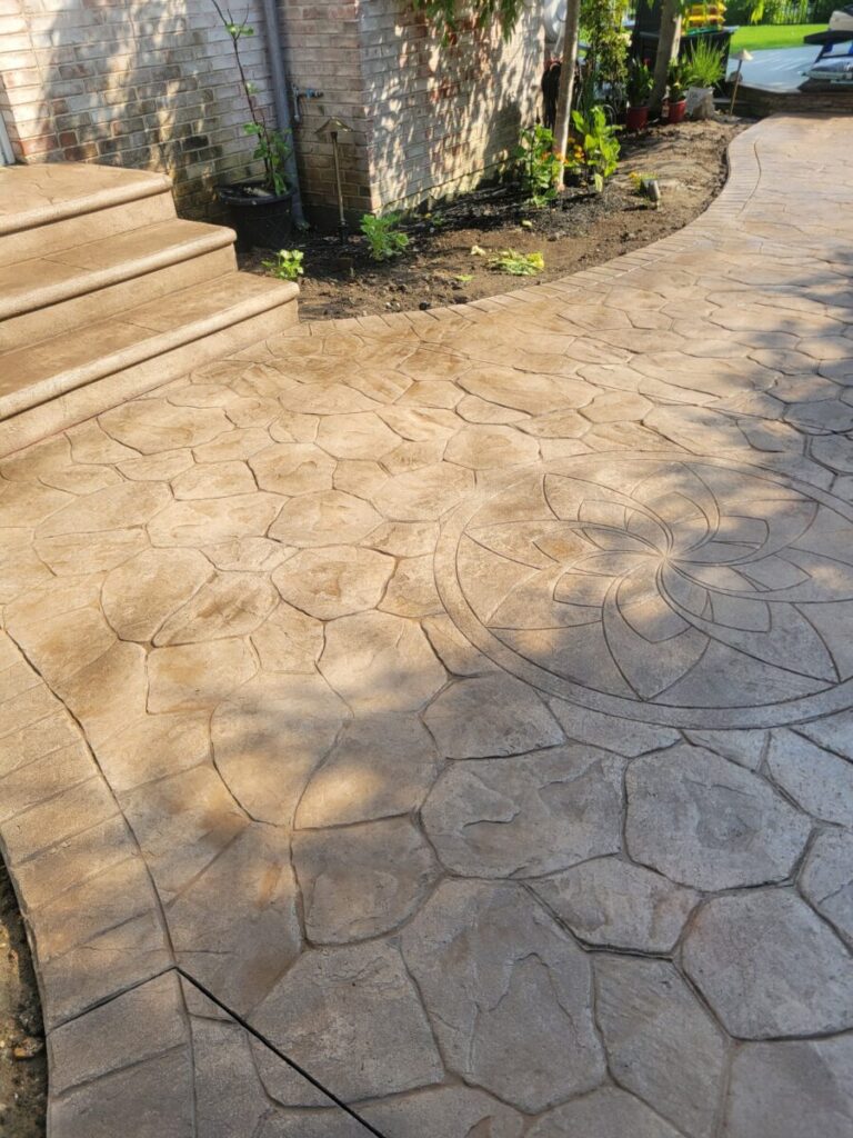 Stamped concrete patio with a geometric and floral pattern near steps and a small garden area.
