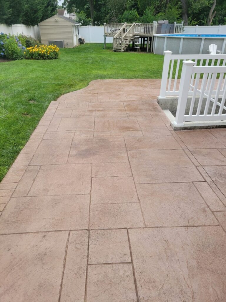 Stamped concrete patio with a white railing, leading to a grassy backyard with a shed and an above-ground pool.
