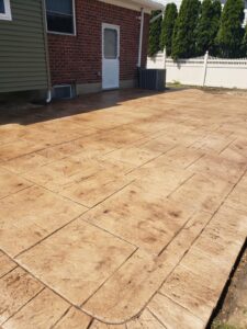 A stamped concrete patio with a rectangular pattern outside a brick house with siding and a white door.