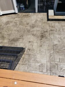 Stamped concrete patio with a metal staircase, wooden railing, propane tank, and sliding glass door in the background.