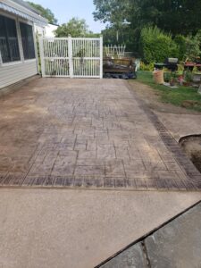 Stamped concrete patio with a brick pattern next to a white fence and garden area in a backyard.