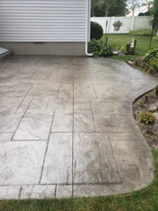 Stamped concrete patio with a geometric pattern beside a house and landscaped garden area.