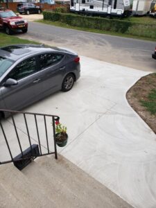 Gray car parked on a concrete driveway next to a sidewalk, with a potted plant on the steps in the foreground.