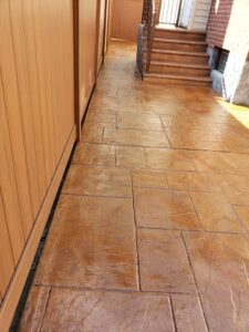 Stamped concrete pathway with a wooden fence on the left, leading to stairs and a doorway at the end.
